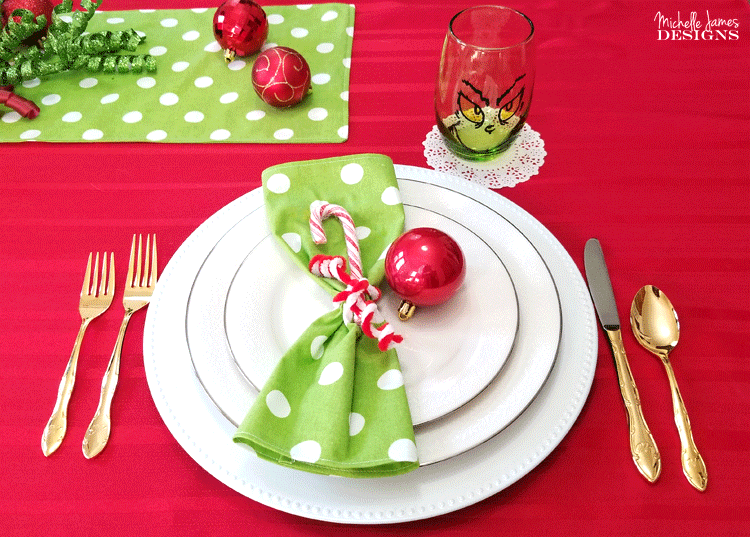 One Place setting with white plates, green with white polka dot napkin, a candy cane and a red Christmas ball.