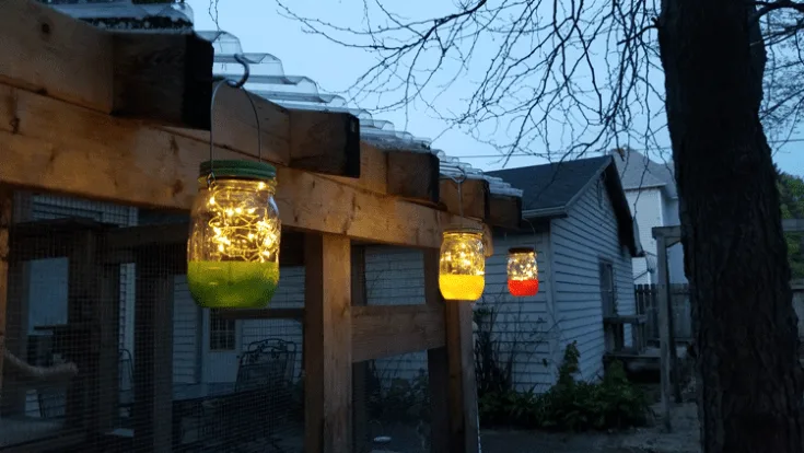 Colorful hanging mason jar solar lights lit up just as it begins to get dark