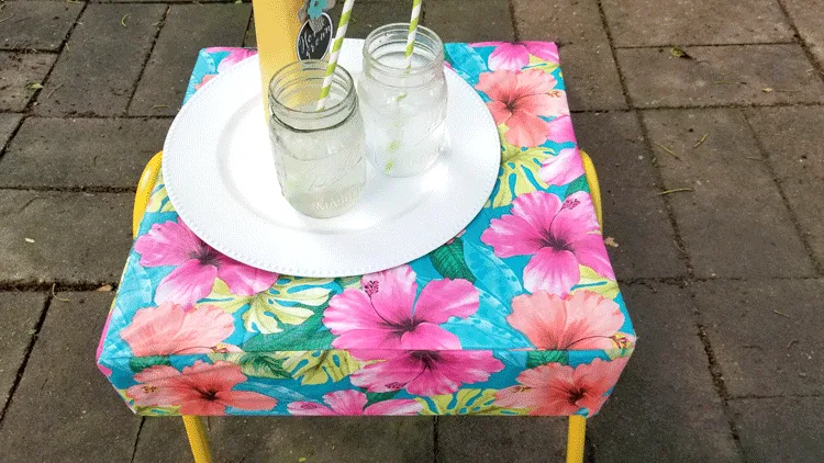 Colorful ottoman in the patio with a tray, water and an upcycled vase with daisies.