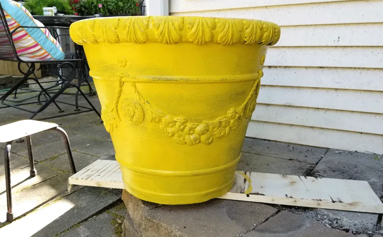 A large foam flower pot after one coat of the harvest yellow color. Some of the black is still showing under the paint. 