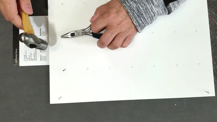 Using a small pair of pliers to hold the nail in order to pound it gently into the board.