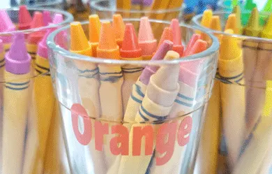 Orange crayons in a glass cup labeled with orange vinyl that says orange.