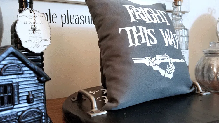 Gray and white "Fright This Way" pillow staged on wood desk with haunted house village and potion bottles