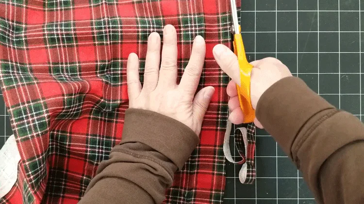 Cutting a plaid fabric strip to wrap around the neck of the glass candle holder