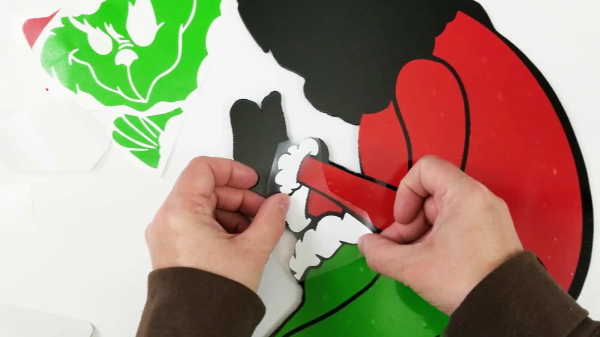 Adding red, white and green vinyl pieces to a black Grinch outline to complete the Grinch yard art
