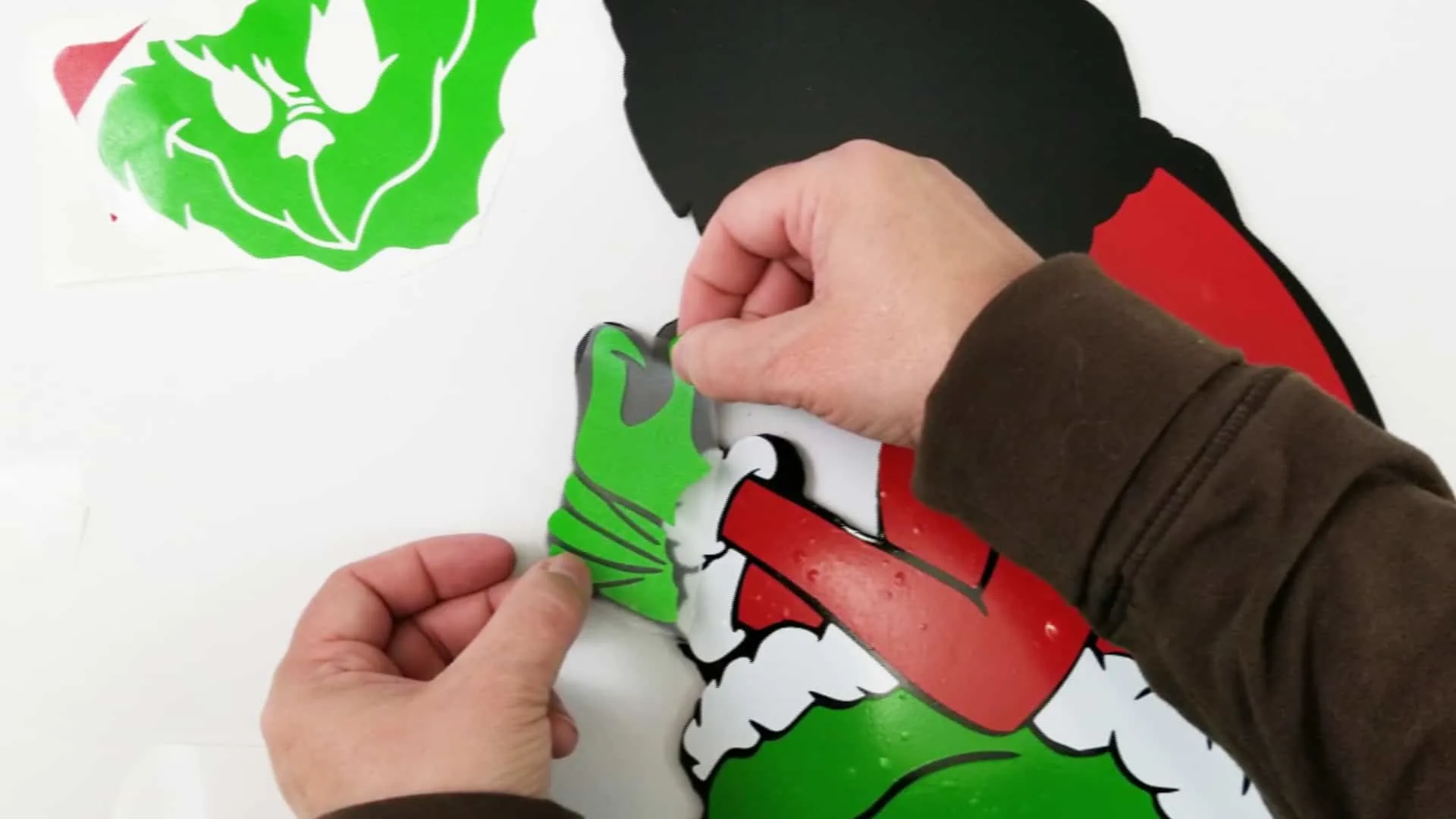 Adding red, white and green vinyl pieces to a black Grinch outline to complete the Grinch yard art