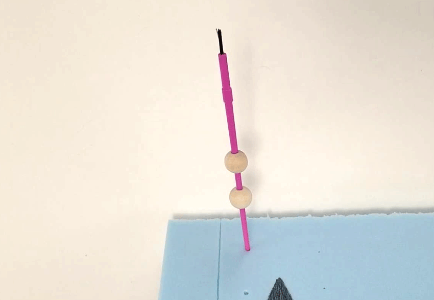 Showing how to dry the painted beads on a paint brush handle stuck in foam
