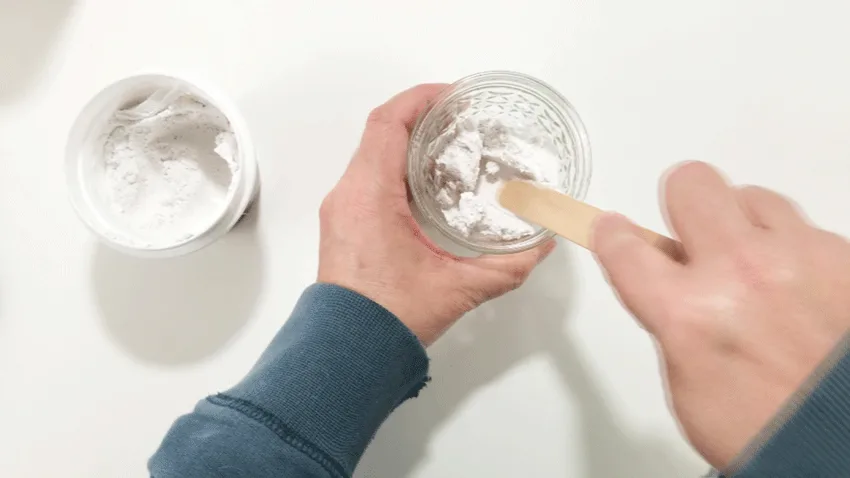 Adding spackle from the container to a jar in order to mix in white paint.