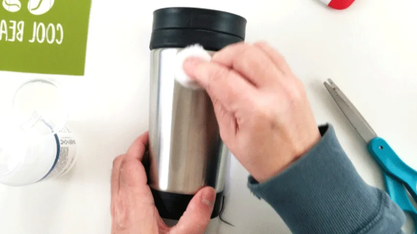 Cleaning the surface of the coffee travel mug with nail polish remover and a cotton ball.