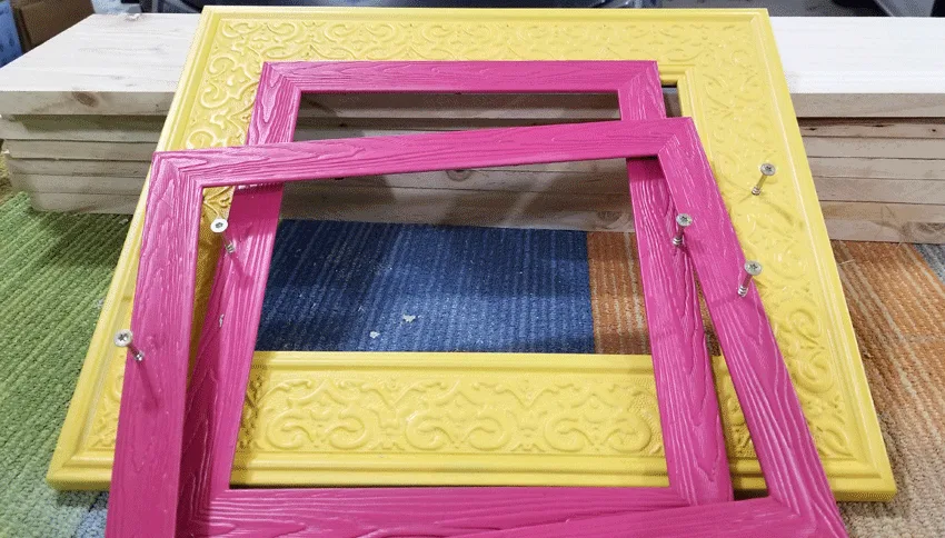 Pink and yellow frames with the screws ready to be hung on the fence.