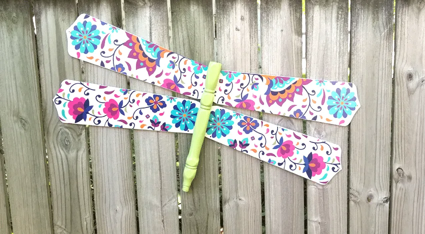 The finished colorful dragonfly DIY wood craft hanging on the fence.