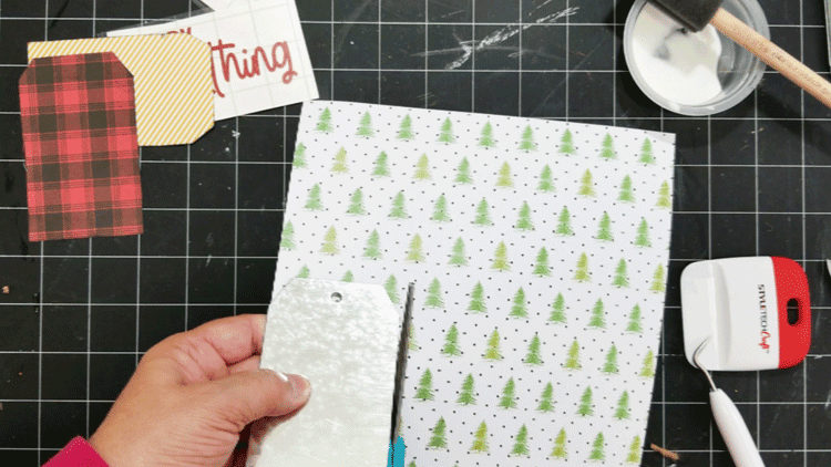 Cutting out the shape of the tag with Christmas pattern paper.