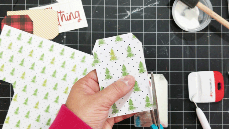 Trimming around the Christmas paper tag to make it slightly smaller than the metal tag.